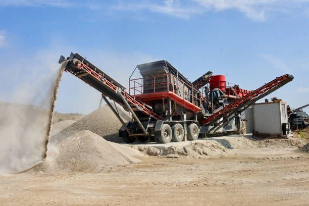 Industrial machine processing sand soil into piles at construction site under blue sky.
