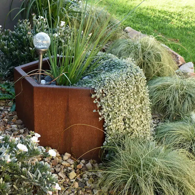 A wooden planter filled with plants and rocks in a garden.