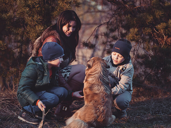 A woman and two children are petting a dog in the woods.