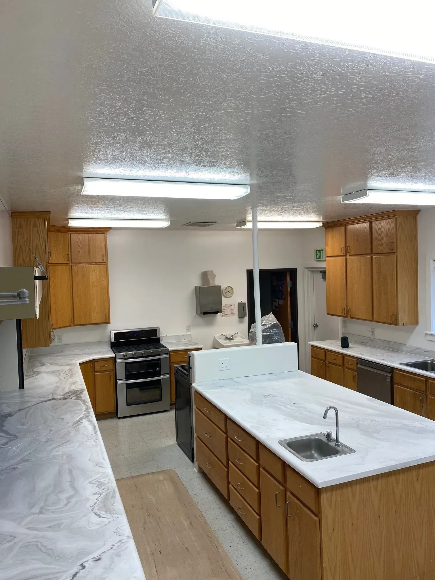 A brightly lit kitchen with wood cabinets, white marble-patterned countertops, a central island with a sink, and a stove.