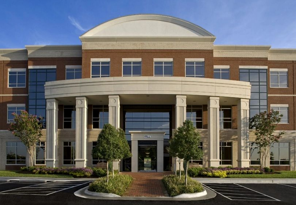 Office building with brick exterior, white columns, glass windows, and a blue sky.