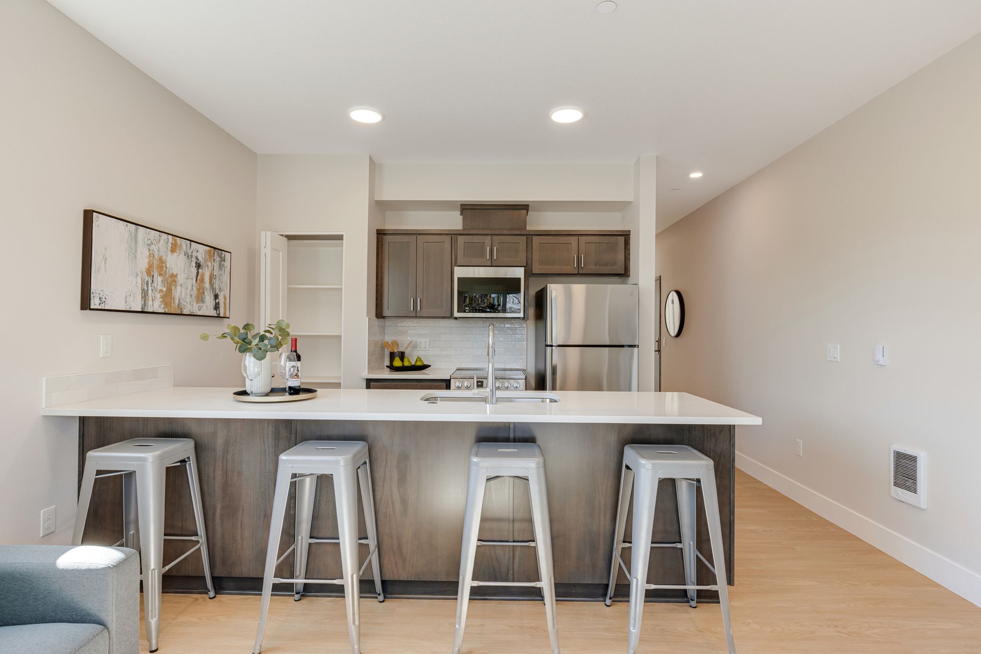 A kitchen with a long island and stools and a refrigerator.