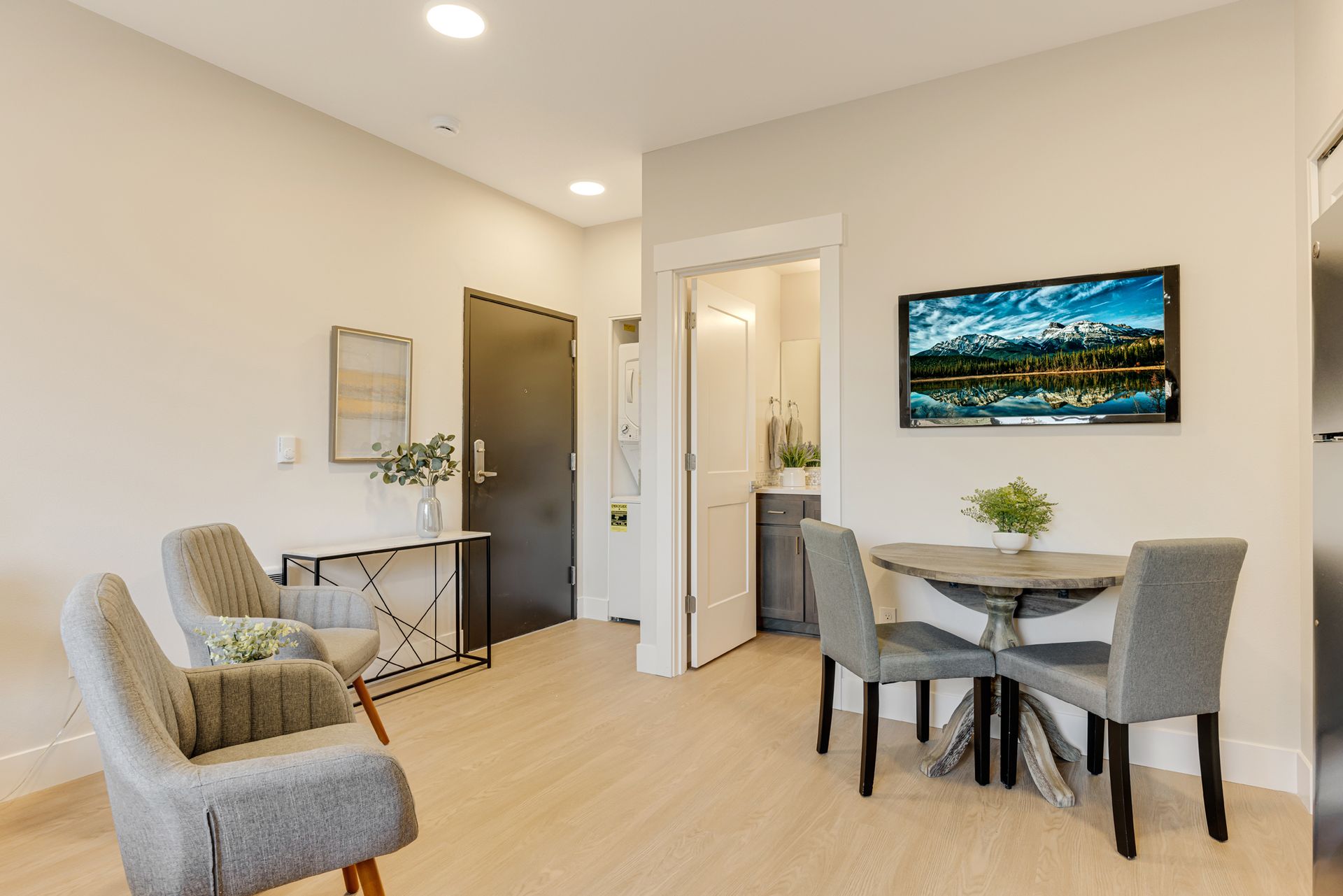 A living room with a table and chairs and a flat screen tv on the wall.