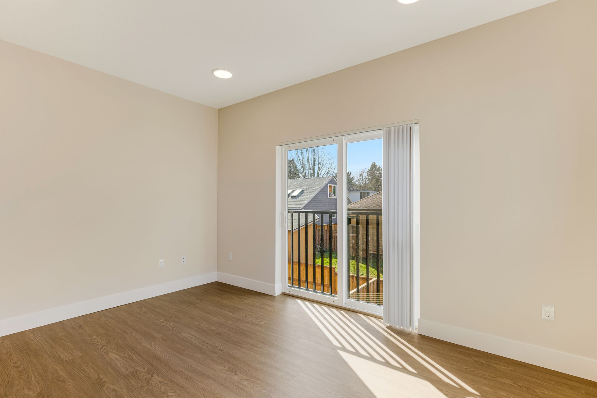 An empty living room with a balcony and sliding glass doors.