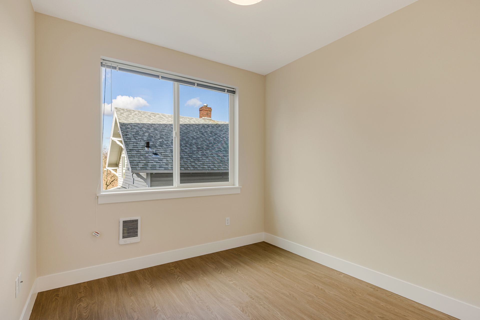 An empty room with a window and hardwood floors.