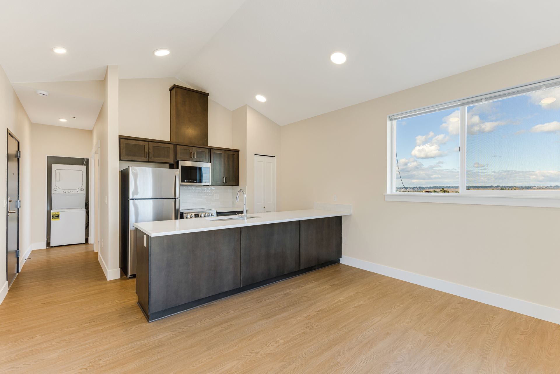 A kitchen with a refrigerator , microwave , sink , and large window.