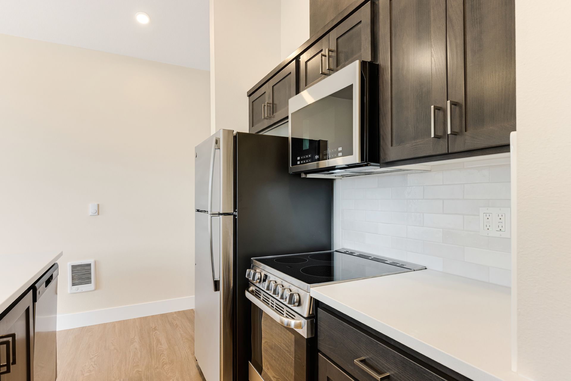 A kitchen with a stove , refrigerator , microwave and cabinets.