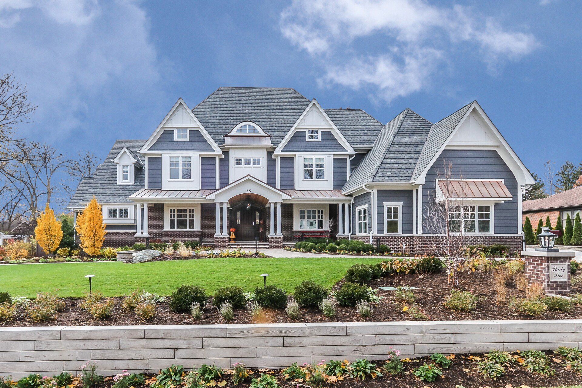 A large gray and white house with a large lawn in front of it.