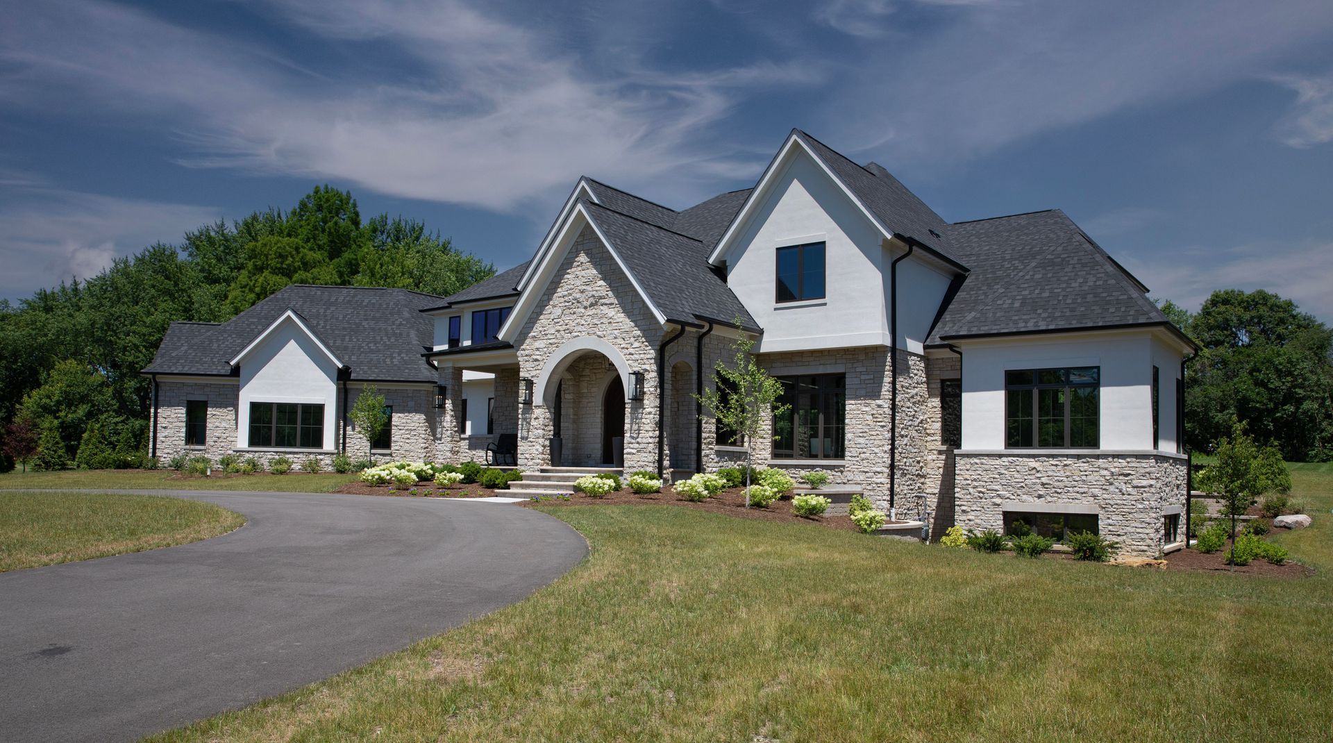 A large white house with a black roof is sitting on top of a lush green field.