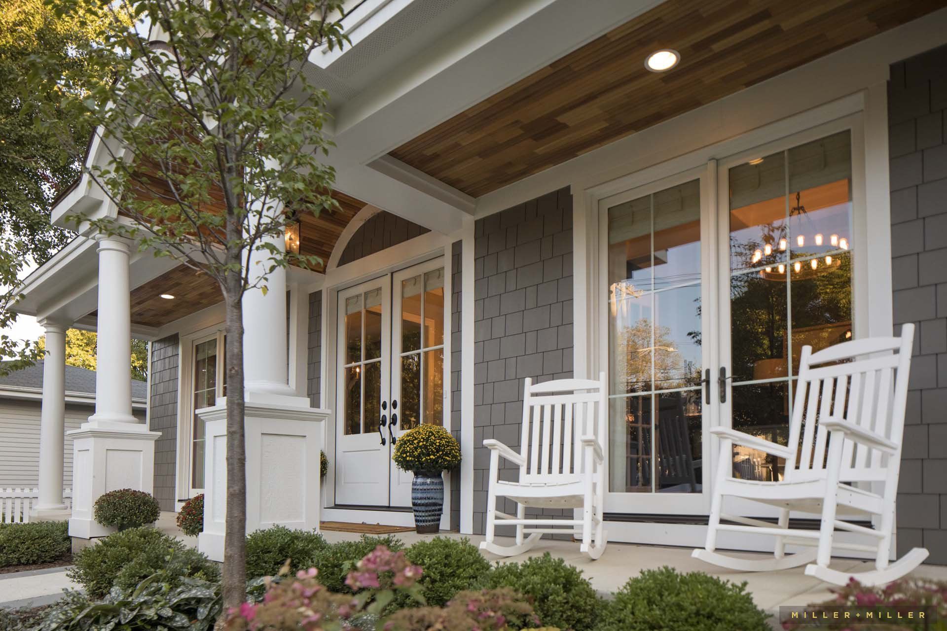 Two white rocking chairs are on the porch of a house