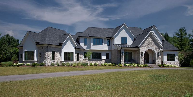 A large white house with a gray roof is sitting on top of a lush green field.