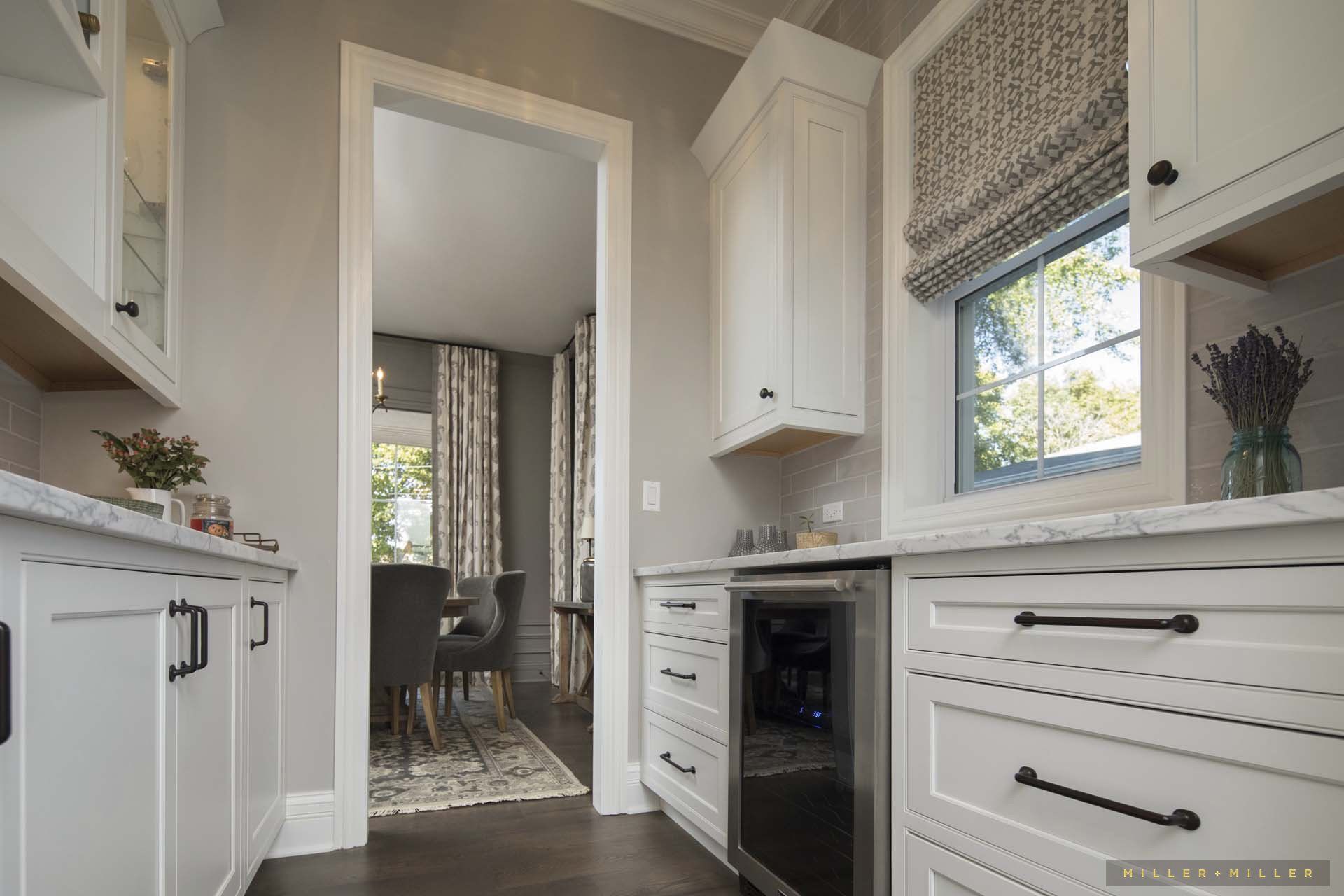 A kitchen with white cabinets , black handles , a refrigerator and a window.