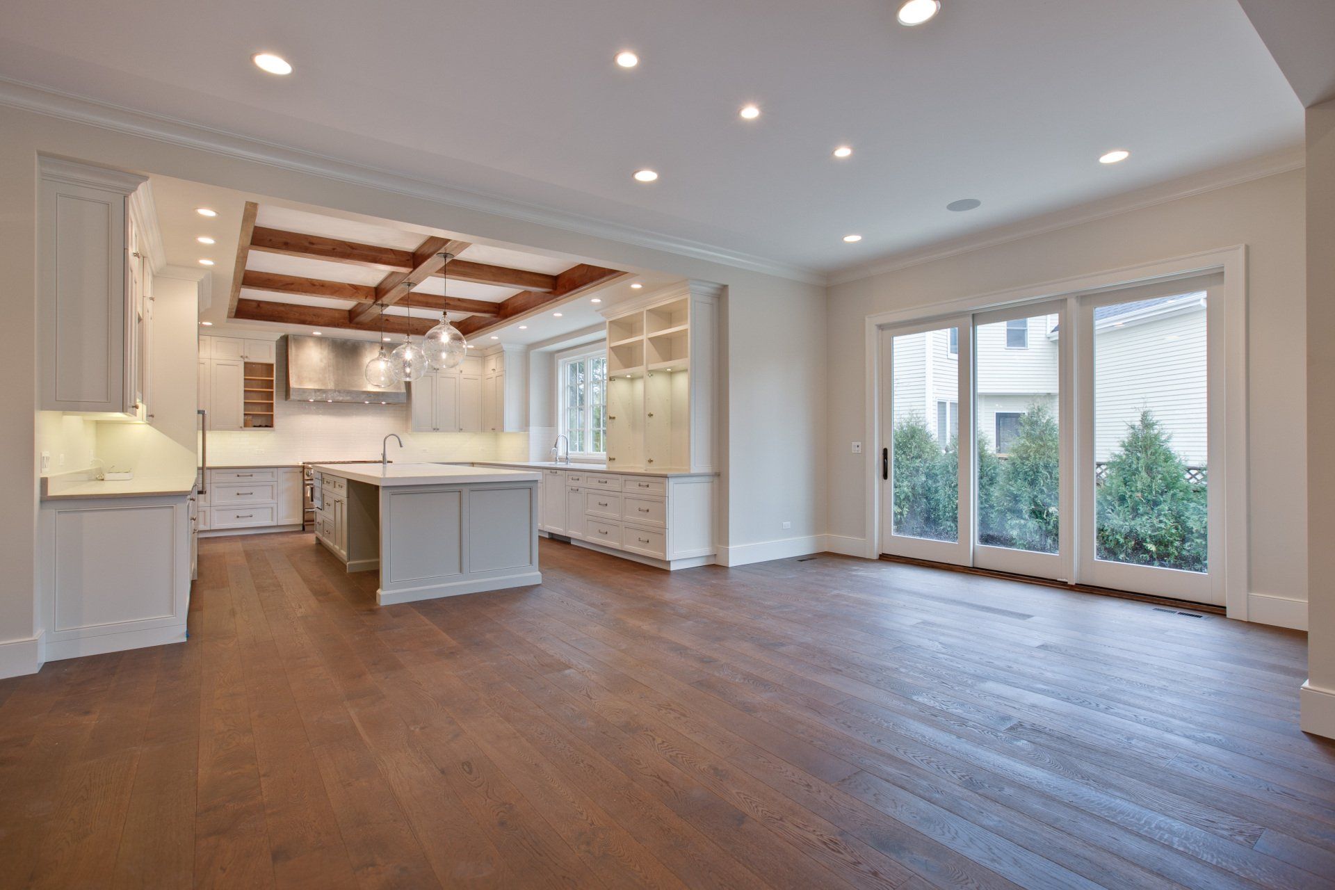 A large empty room with hardwood floors and a kitchen in the background.