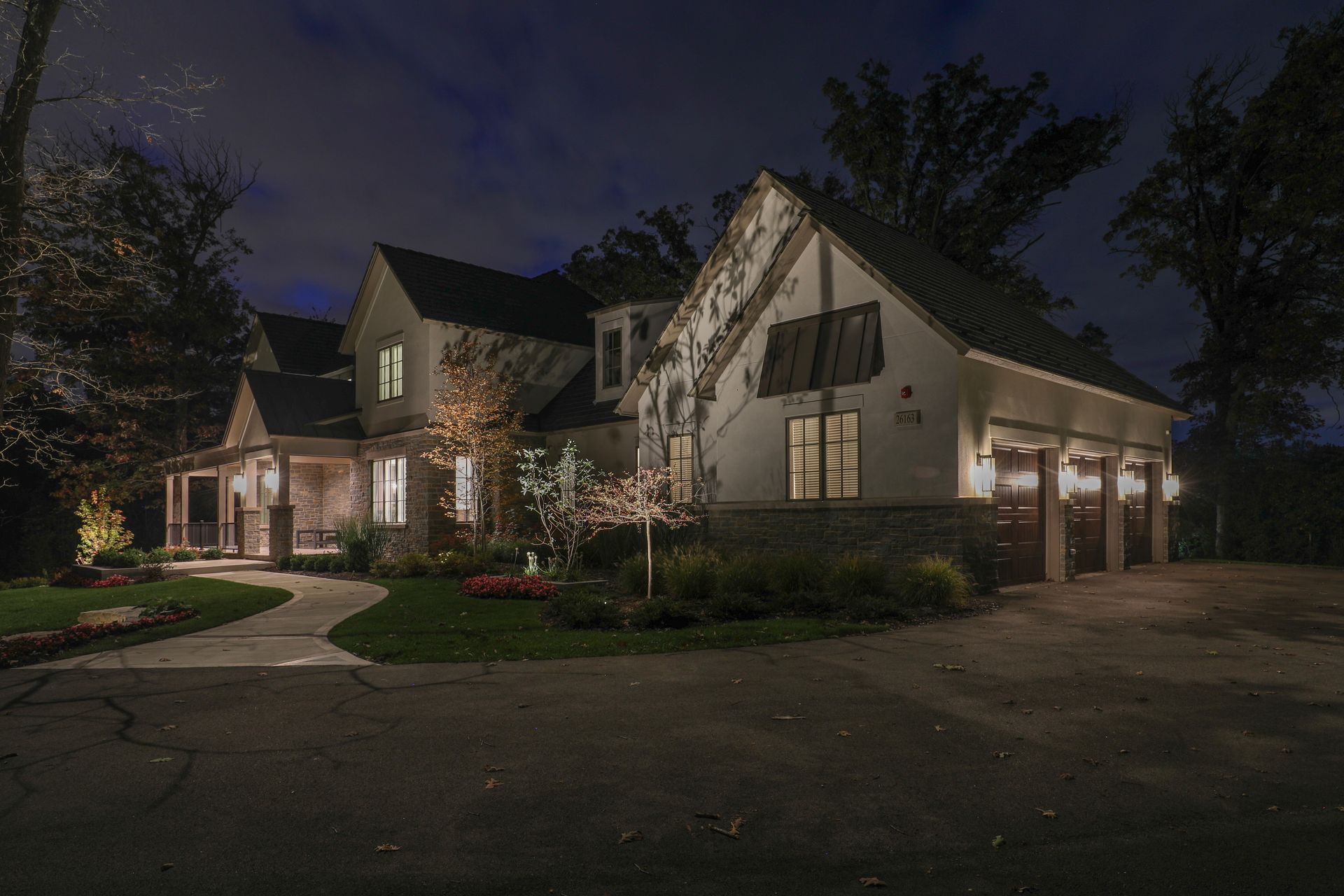 A large white house with a garage is lit up at night