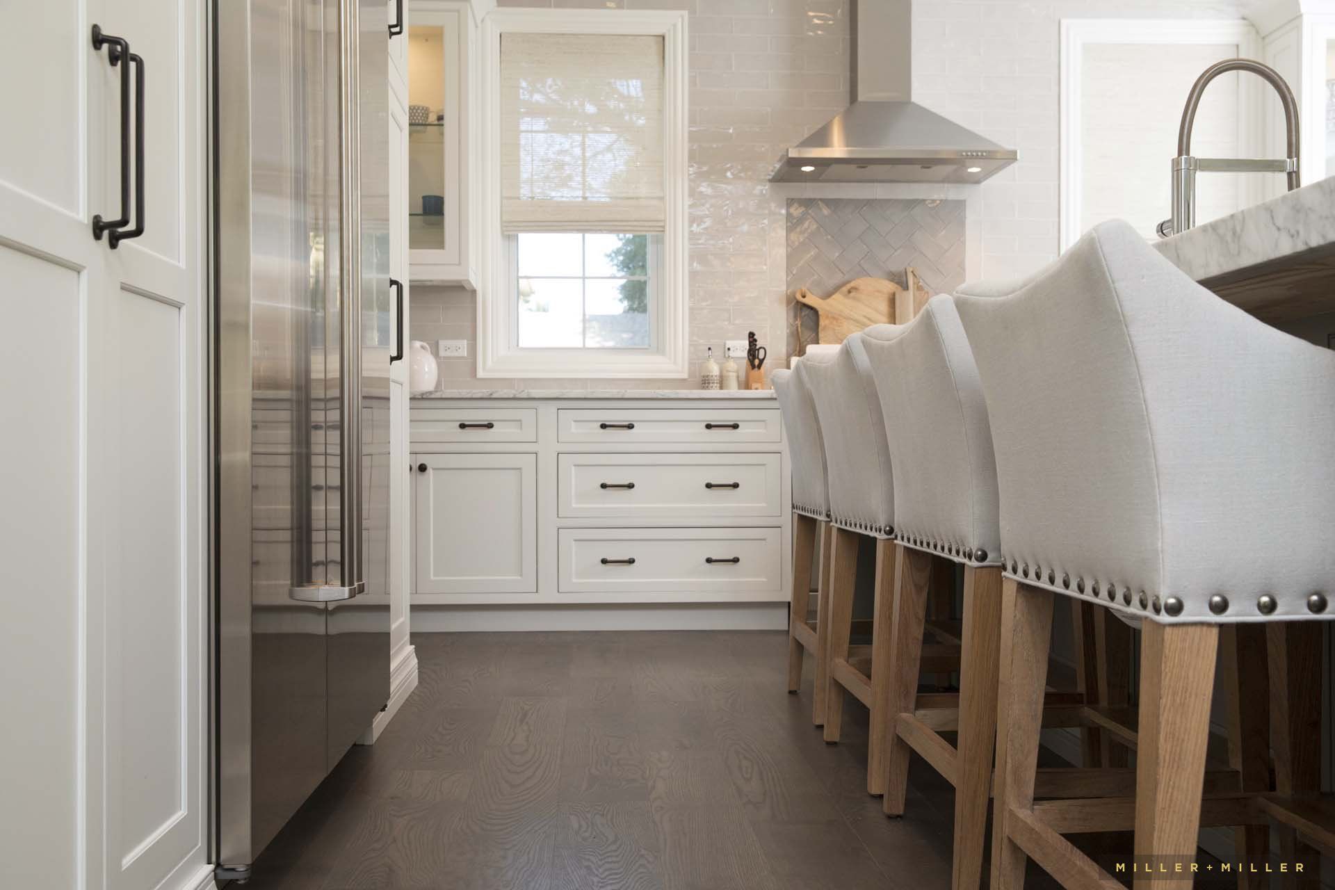 A kitchen with white cabinets and stools and a stainless steel refrigerator