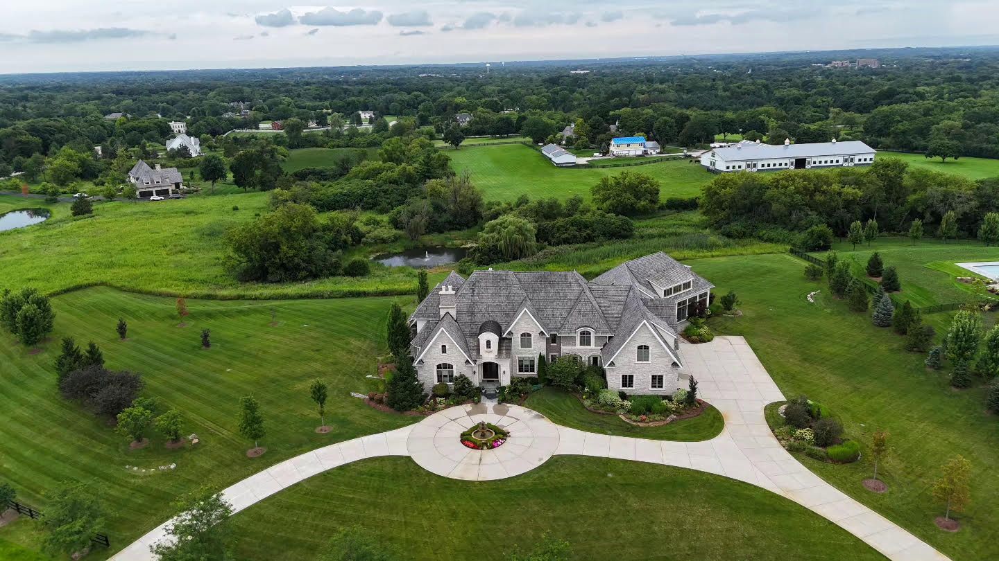 An aerial view of a large house in the middle of a lush green field.