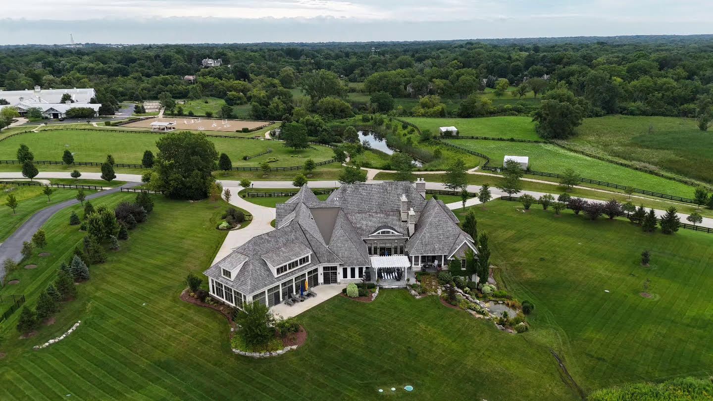 An aerial view of a large house in the middle of a lush green field.