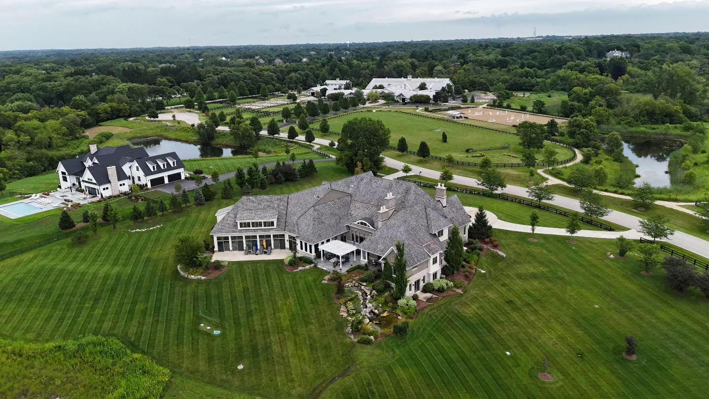An aerial view of a large house in the middle of a lush green field.