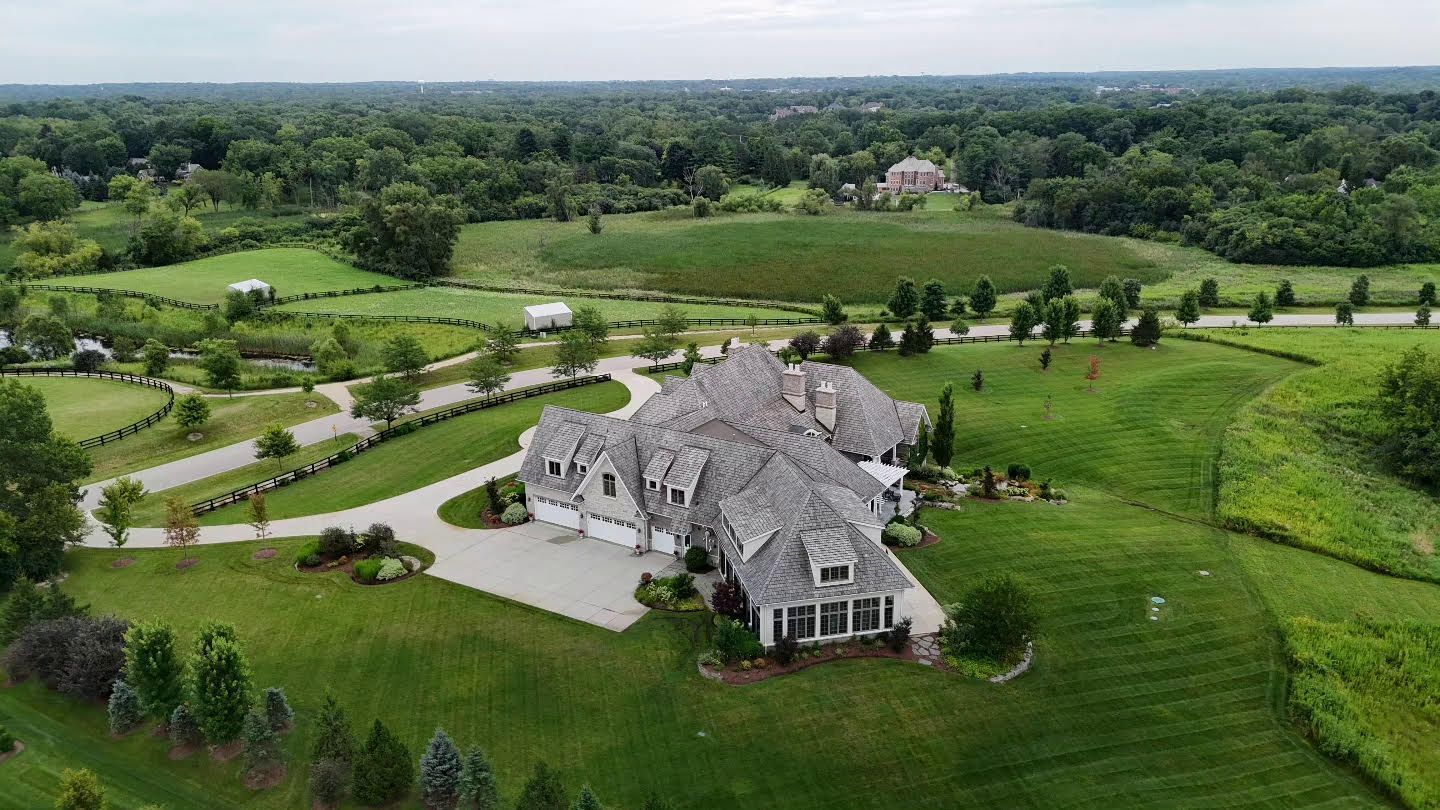 An aerial view of a large house in the middle of a lush green field.
