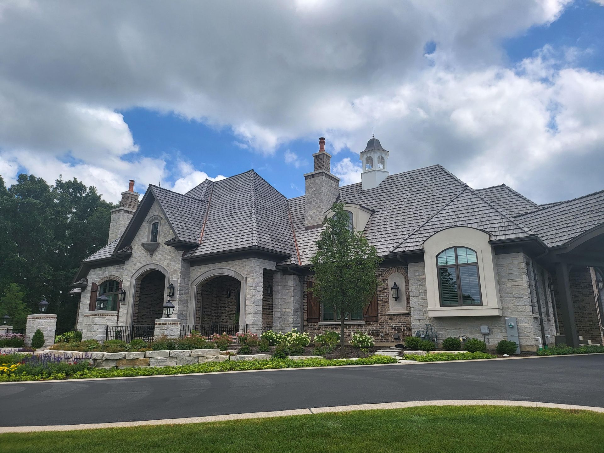 A large house with a gray roof is sitting on top of a lush green field.