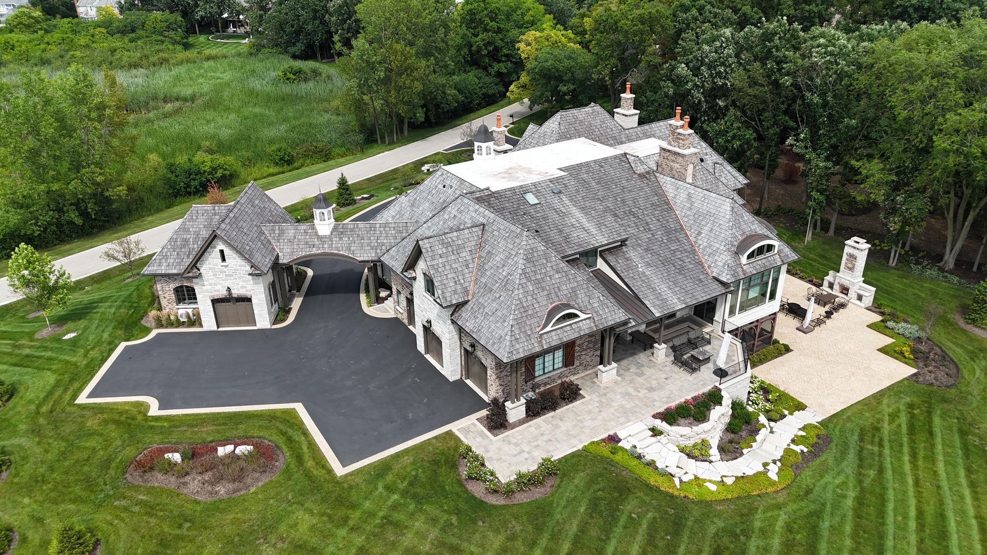 An aerial view of a large house with a large driveway surrounded by trees.