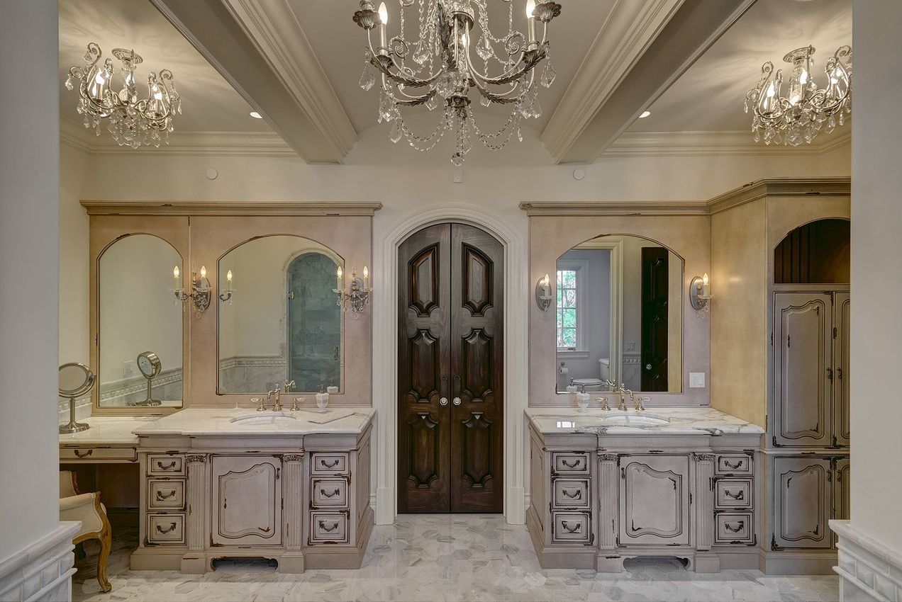 A bathroom with two sinks , two mirrors and a chandelier.