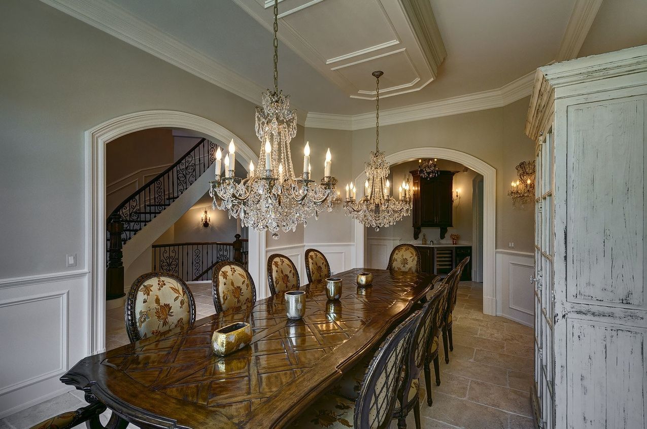 A dining room with a long table and chairs and chandeliers hanging from the ceiling.