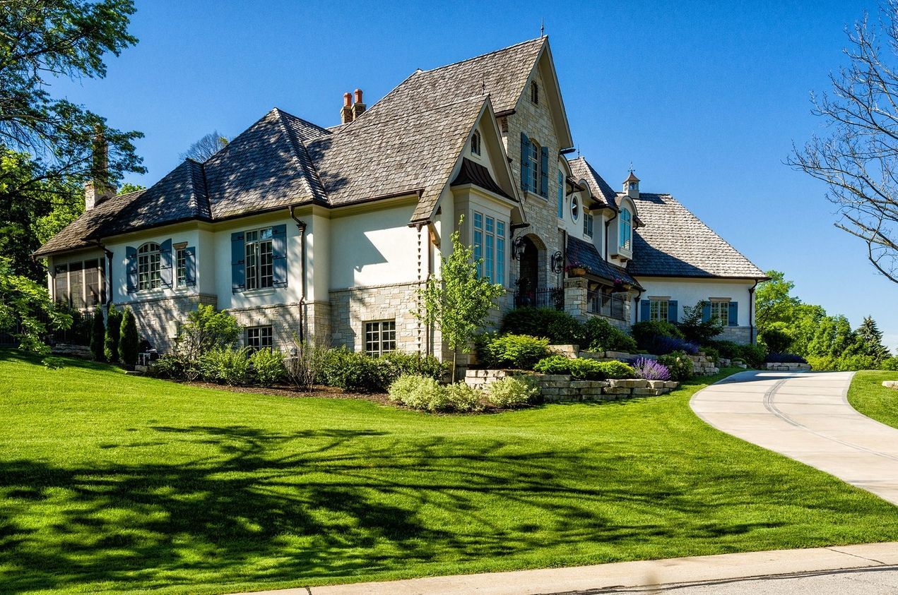 A large house with a lush green lawn and a driveway leading to it.