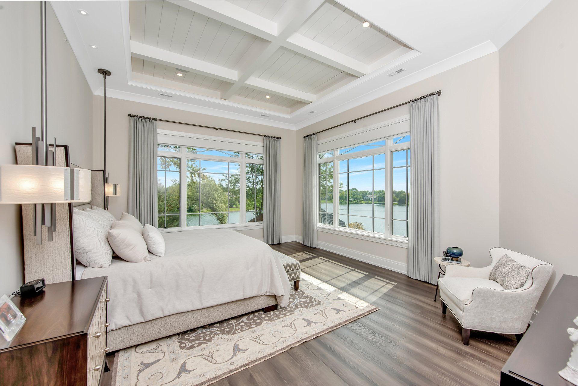 A bedroom with a large bed , chair , nightstand and lots of windows.