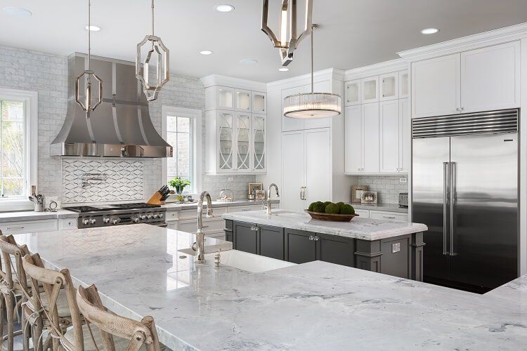 A kitchen with white cabinets , marble counter tops , stainless steel appliances and a large island.