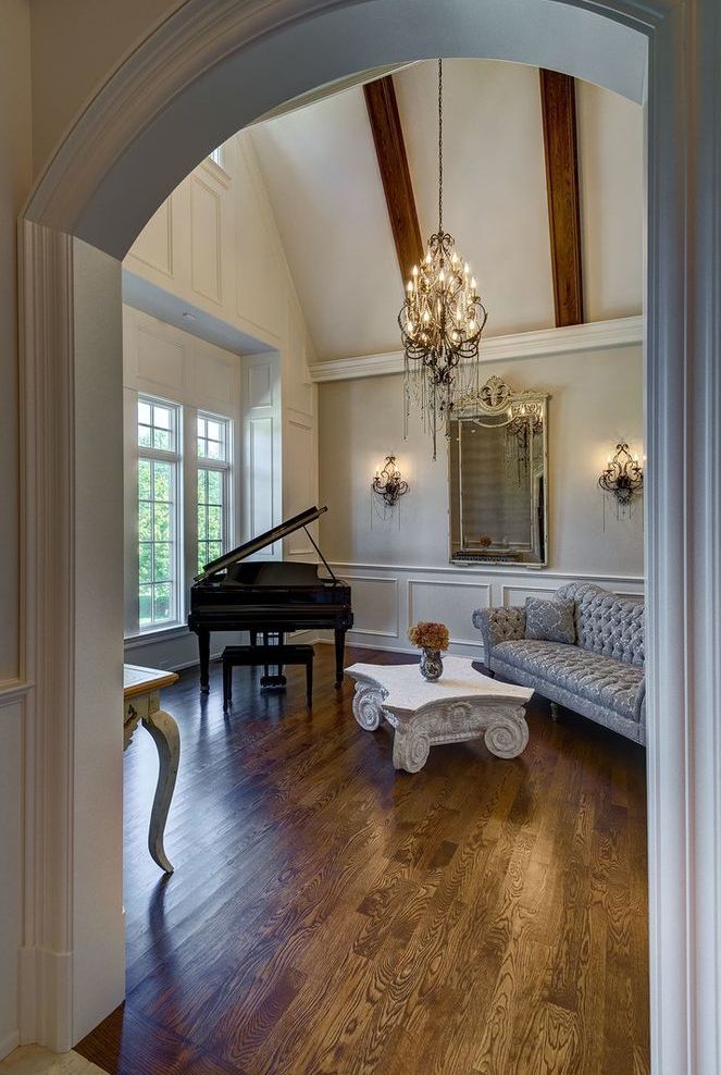 A living room with a piano , couch , coffee table and chandelier.