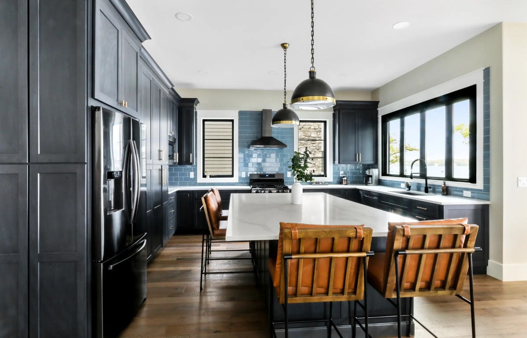 A kitchen with black cabinets , stainless steel appliances , a large island and chairs.