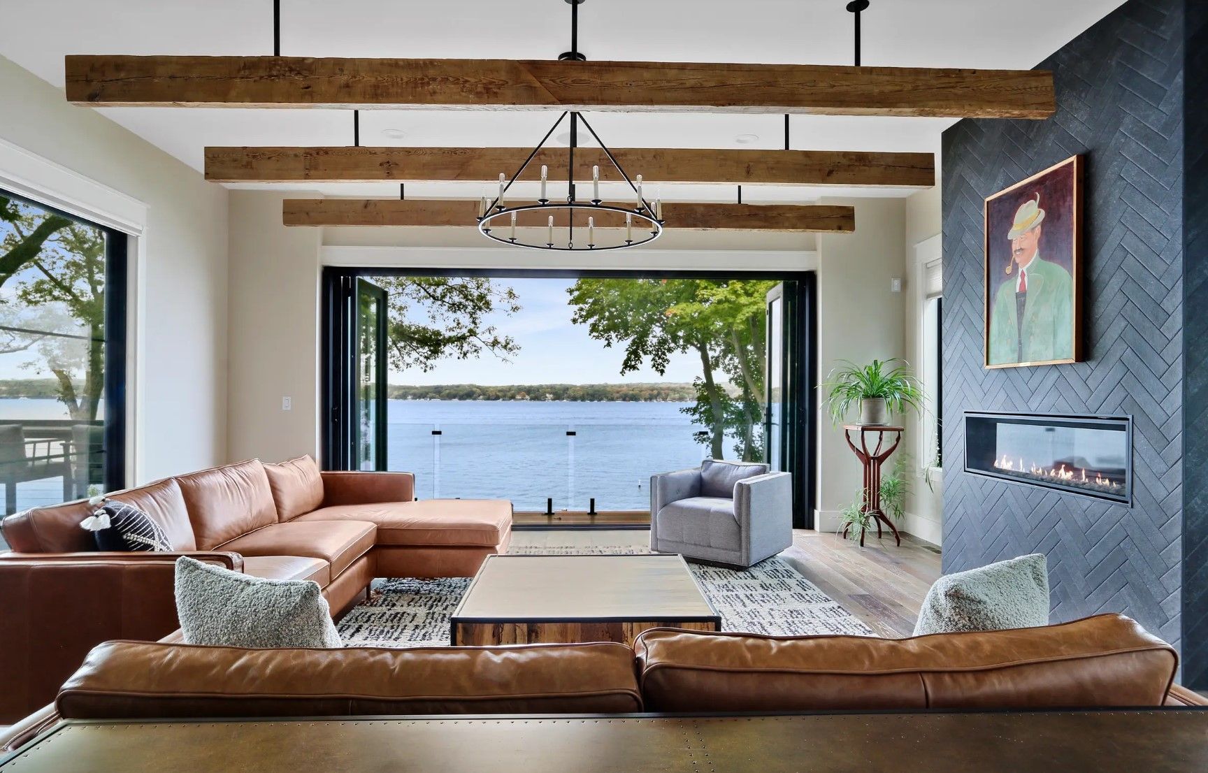 A living room with a couch , chair , table and fireplace overlooking a lake.
