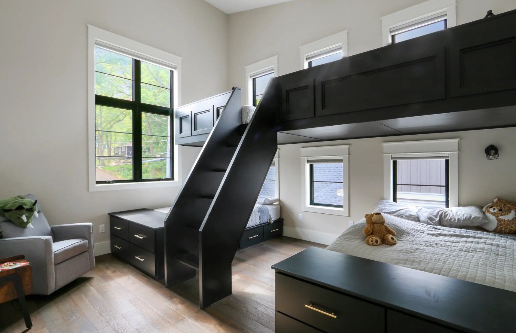 A bedroom with a bunk bed , dresser , chair and stairs.