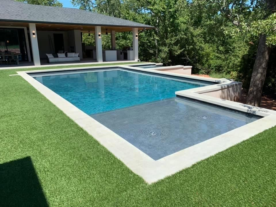 A large swimming pool is surrounded by grass in front of a house.