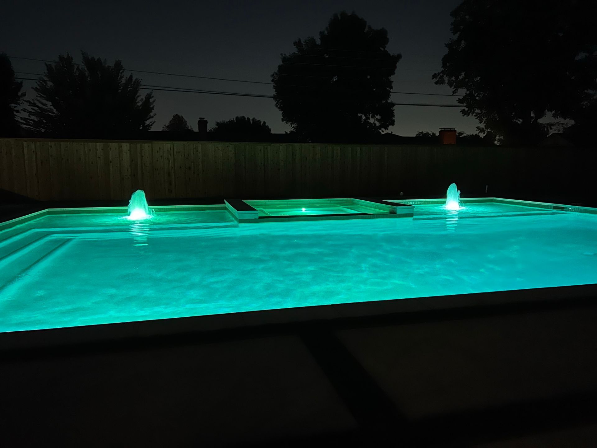 A swimming pool is lit up at night with green lights