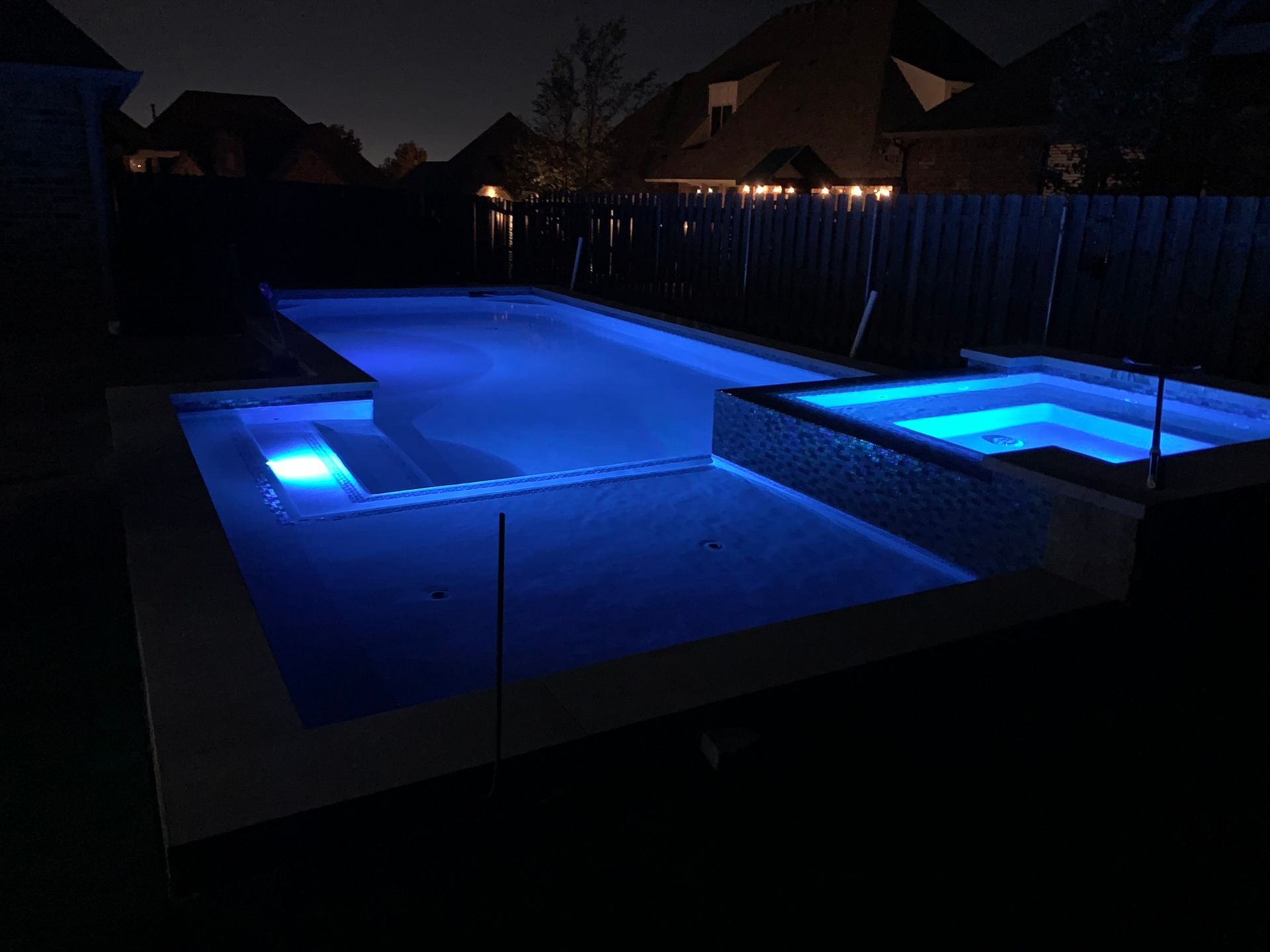 A large swimming pool is lit up at night with blue lights.