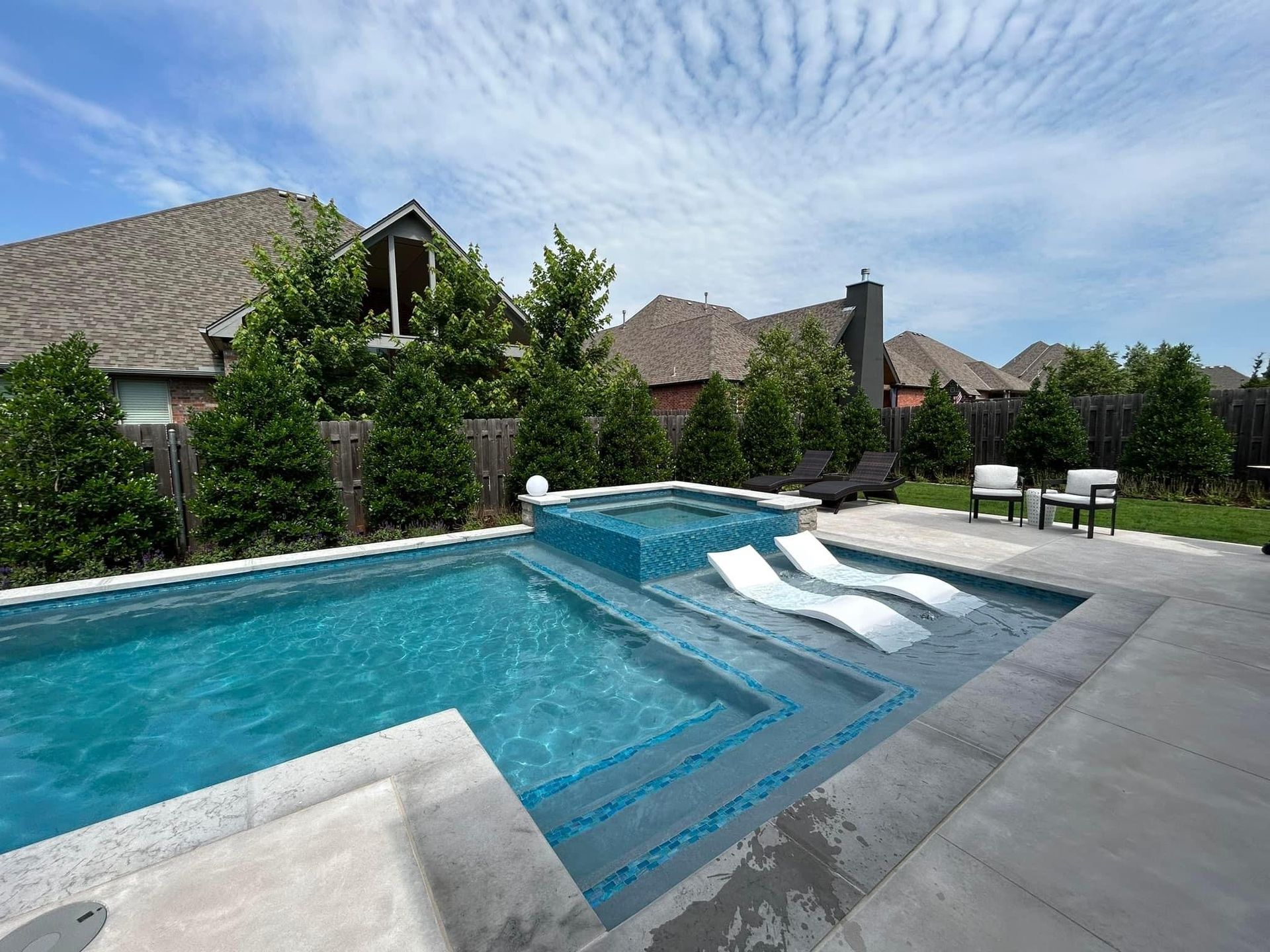A large swimming pool is surrounded by a fence and chairs.