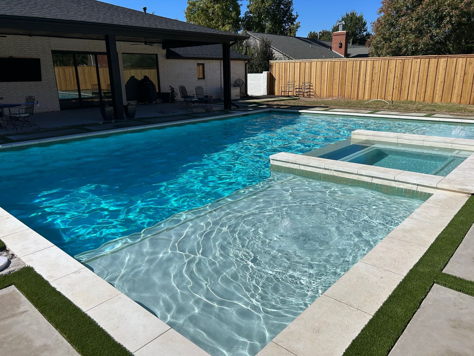 A large swimming pool with a hot tub in the backyard of a house.