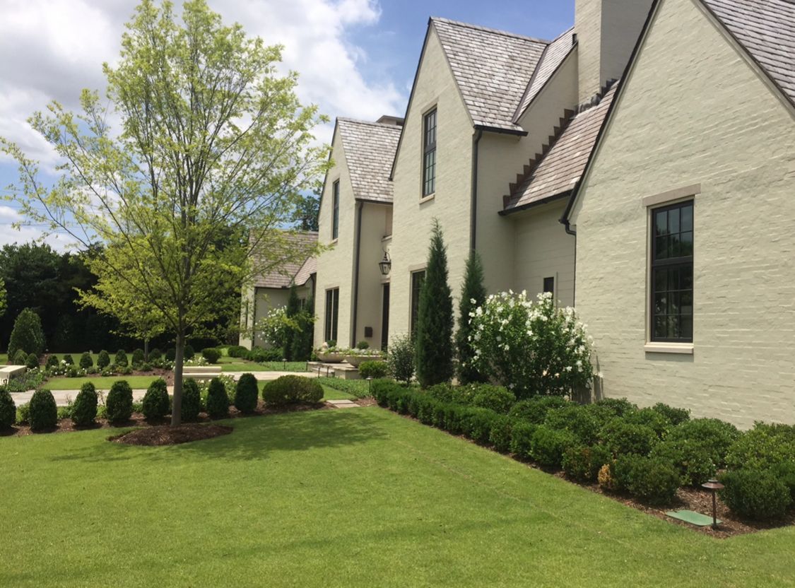 A large white brick house with a lush green lawn in front of it.