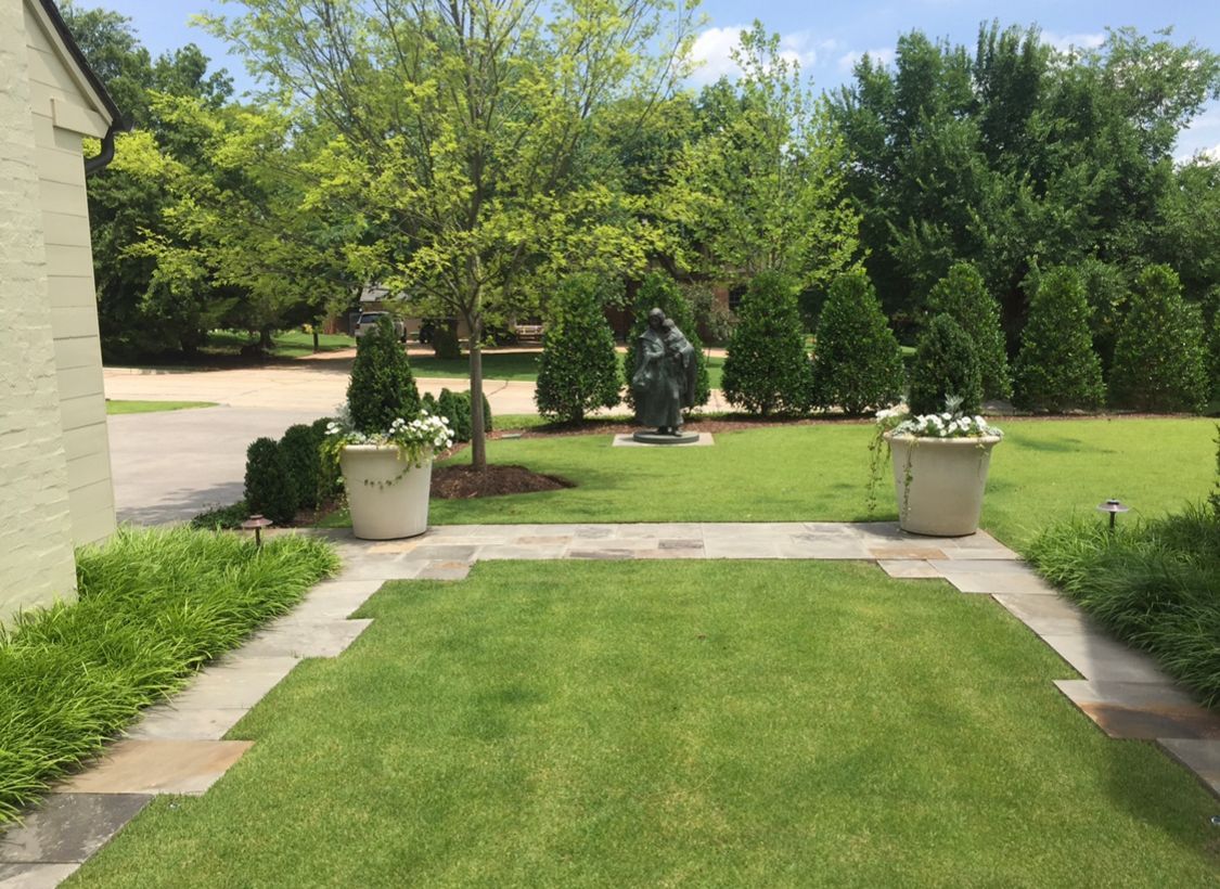 A lush green lawn with a stone walkway leading to a house.
