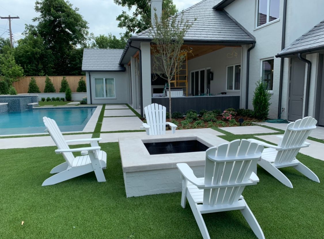 A lawn with chairs and a fire pit in front of a house.