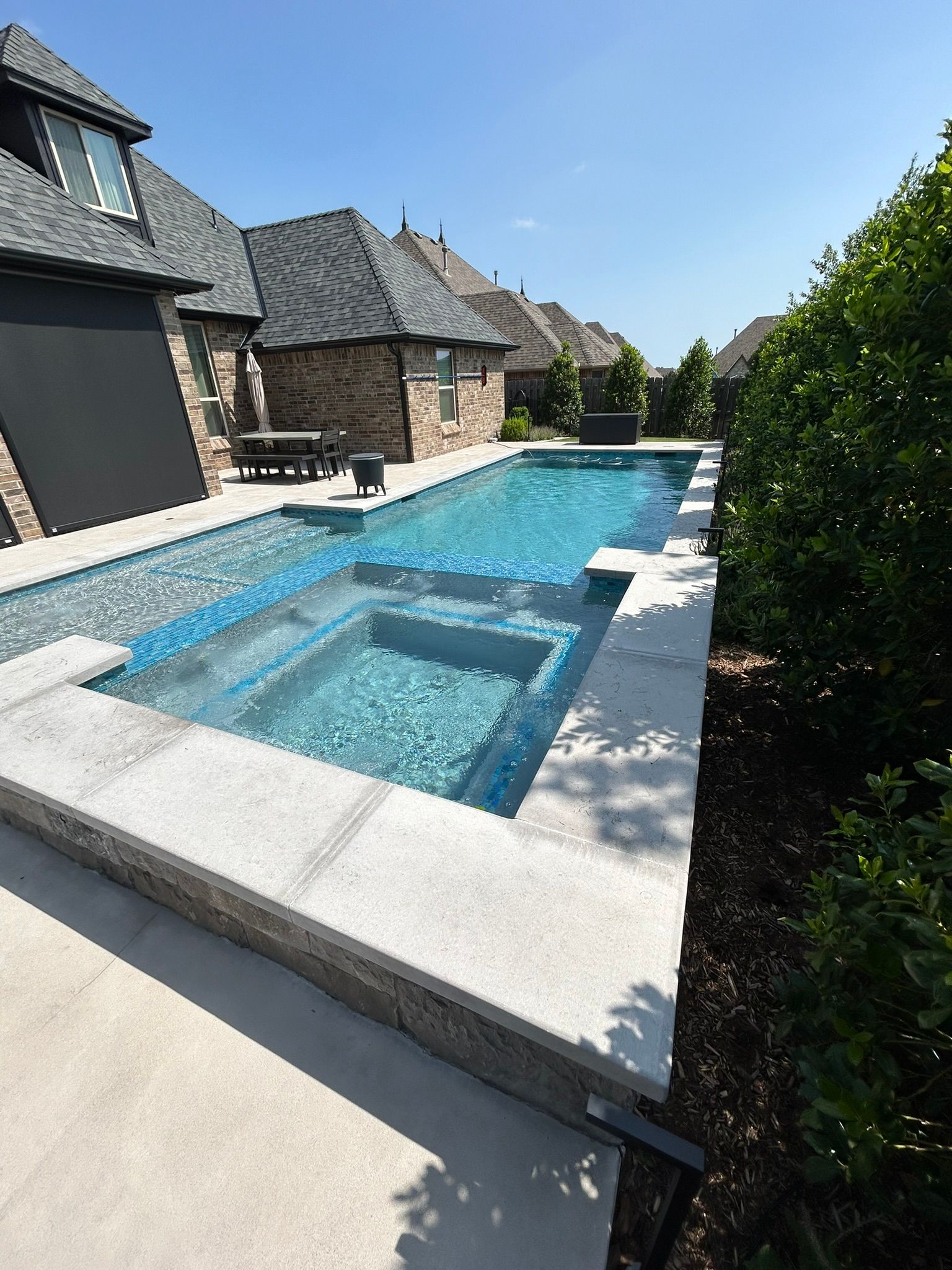 A large swimming pool with a hot tub in the backyard of a house.