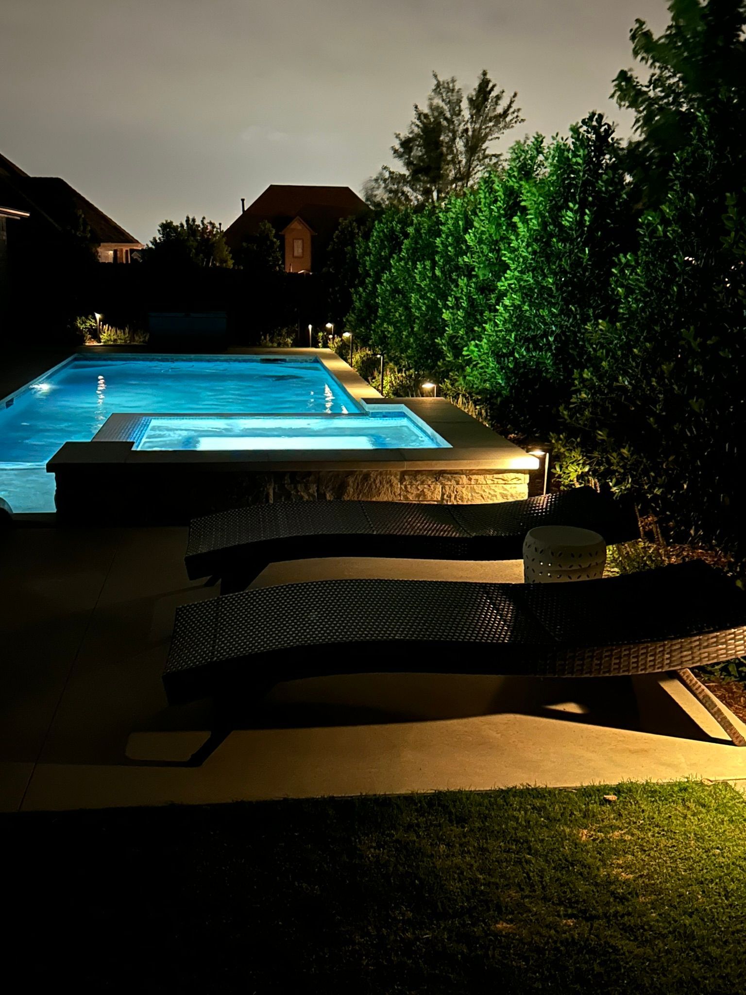 A large swimming pool is lit up at night in a backyard.