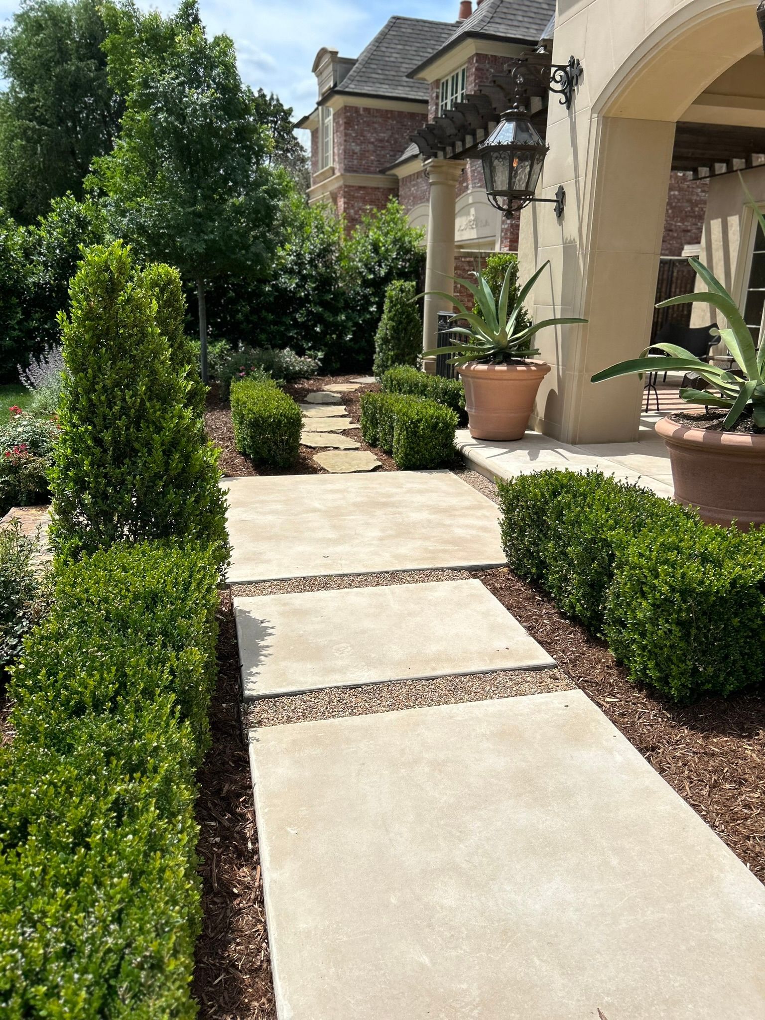 A concrete walkway leading to a house surrounded by trees and bushes.
