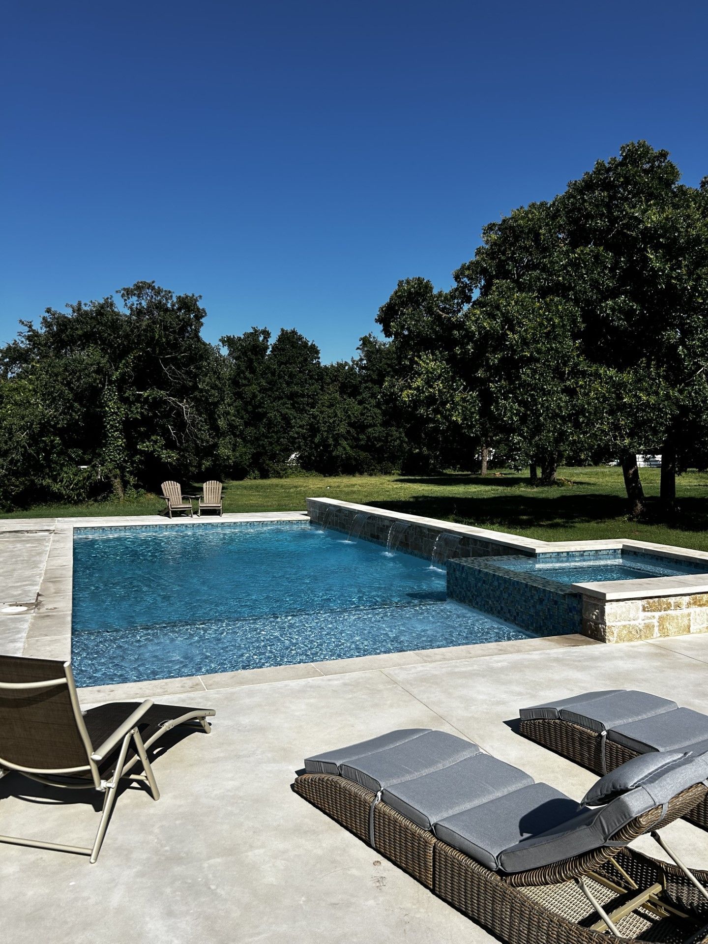 A large swimming pool surrounded by chairs and trees on a sunny day