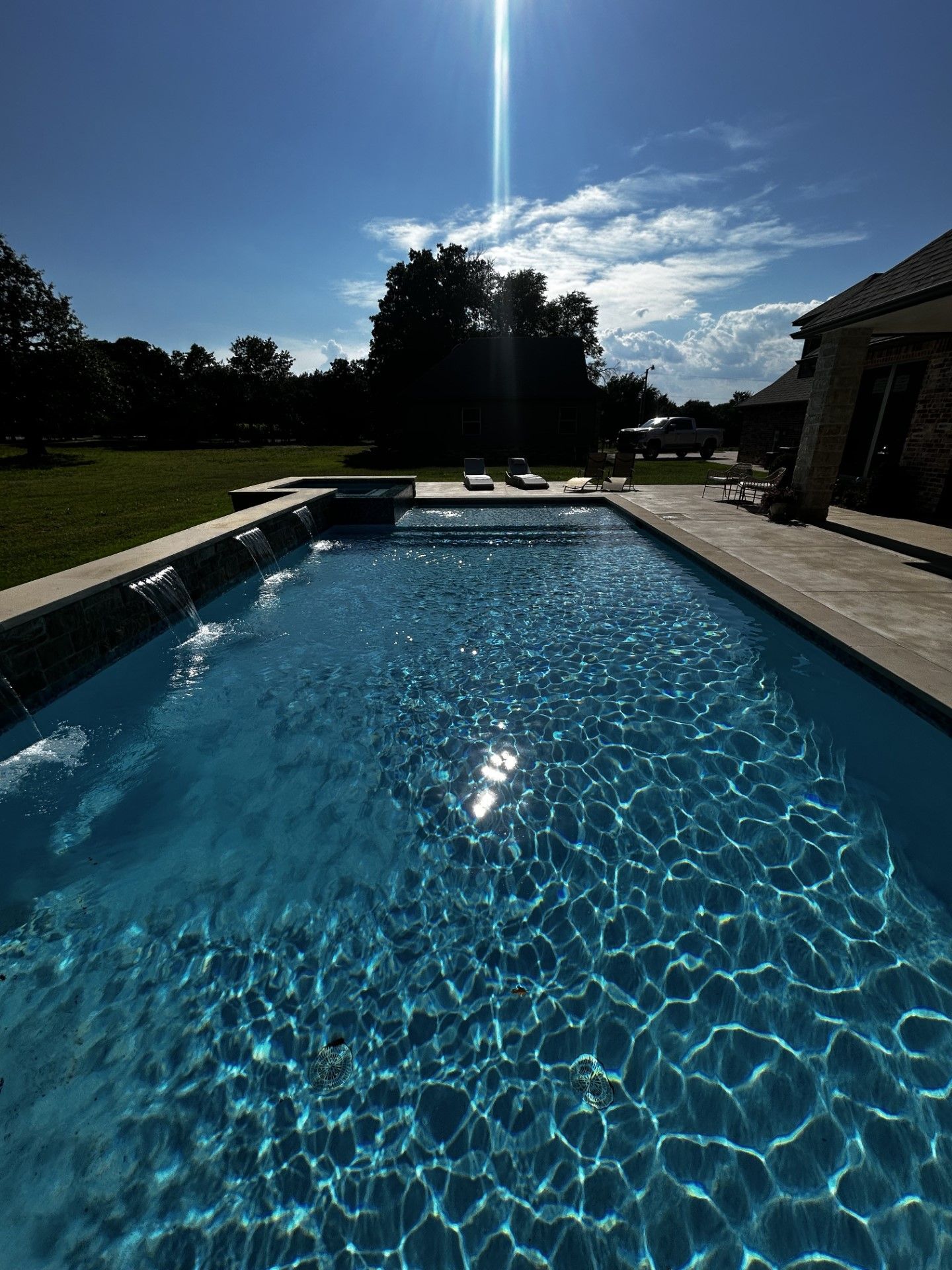 A large swimming pool with a waterfall in the backyard on a sunny day.