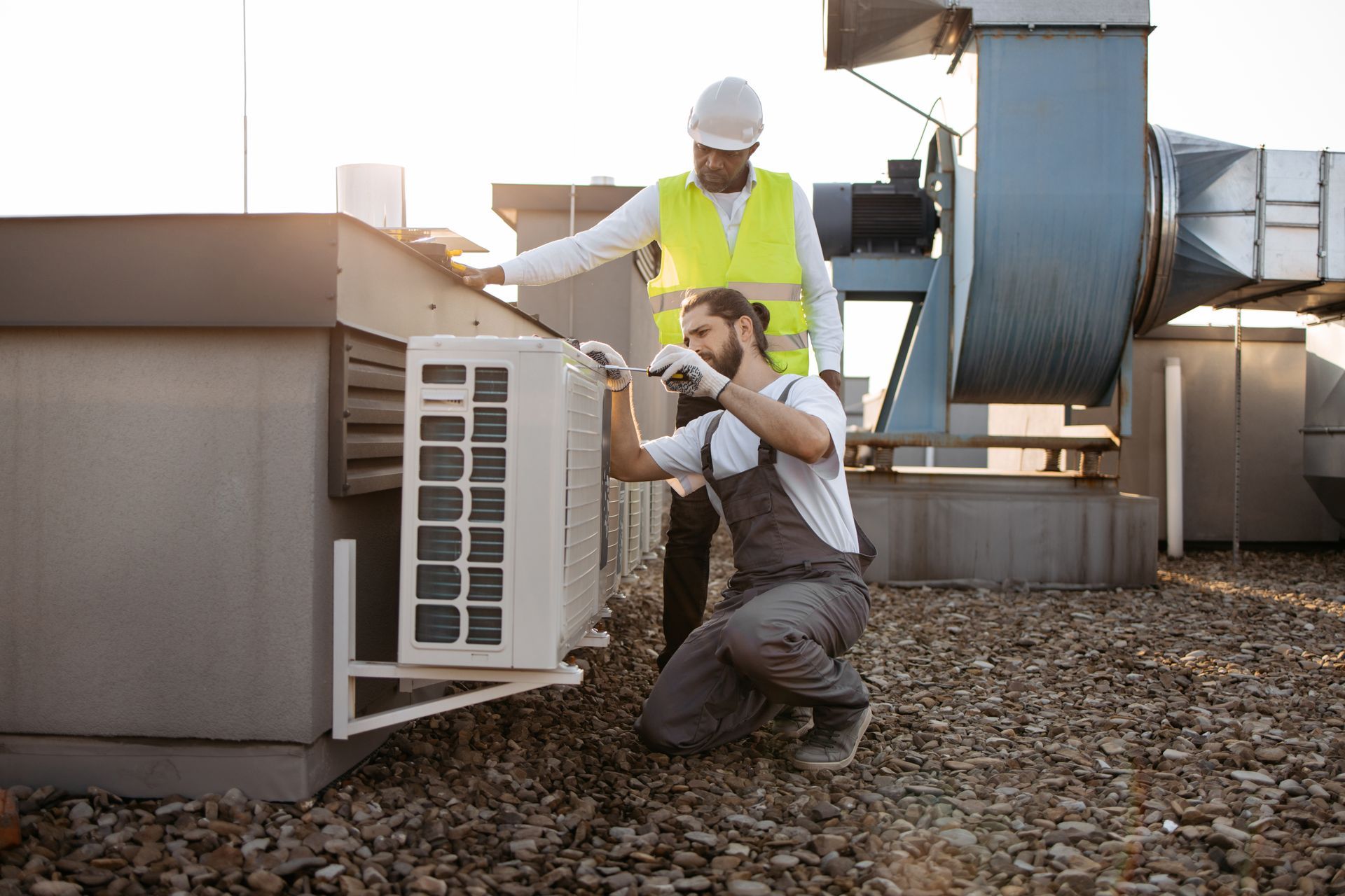 Two men are working on an air conditioner on the roof of a building.
