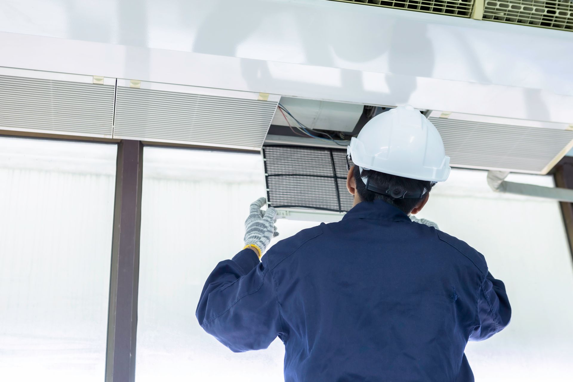 A man wearing a hard hat is working on a ceiling fan
