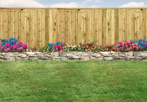 A wooden fence with flowers in front of it and a stone wall.